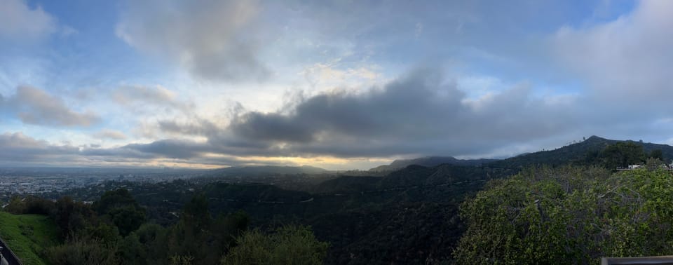 A panoramic view of Los Angeles and the Hollywood hills from the Griffith Observatory under a cloudy sunset.